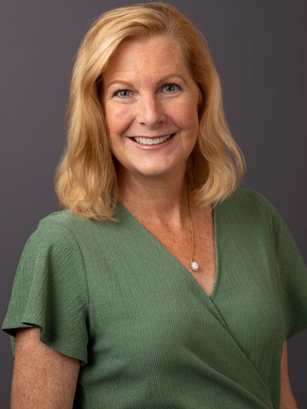 Smiling woman with blonde hair wearing a green blouse and a necklace.