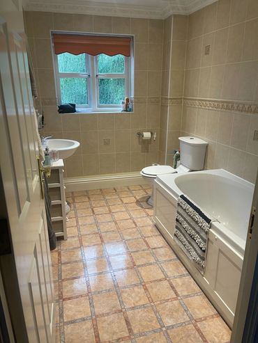 Neat bathroom with beige tiles, bathtub, toilet, and a window with an orange blind.