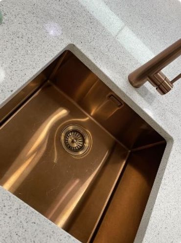 A shiny bronze kitchen sink with a modern faucet on a speckled countertop.