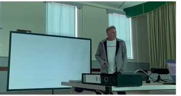 Man giving a presentation in a room with a projector screen and laptop.