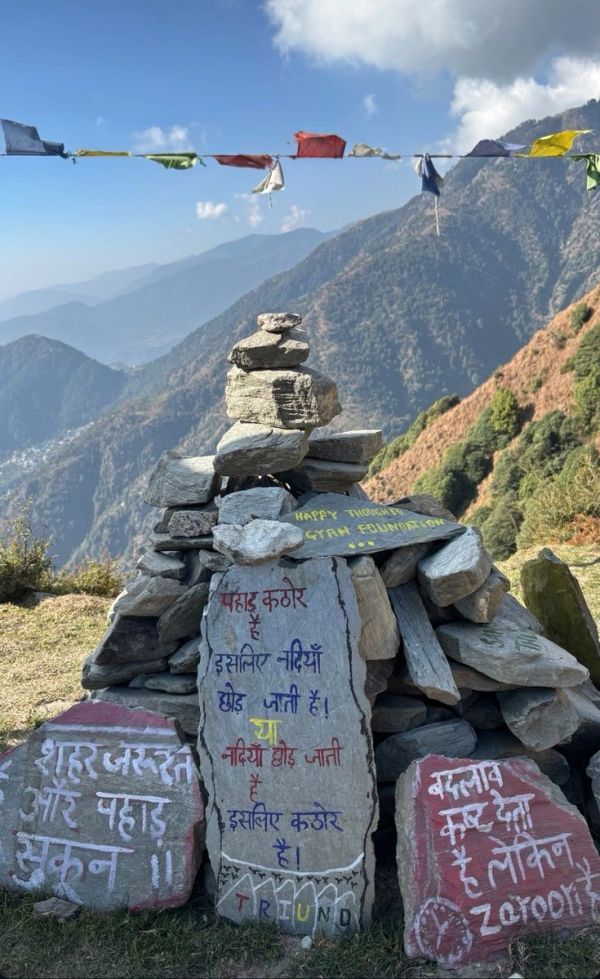 Mountain rocks with Hindi text and prayer flags in the background.
