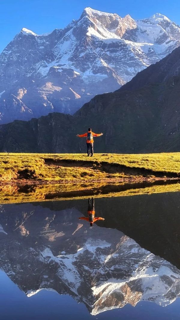 Person with arms outstretched in front of a snowy mountain with reflection.