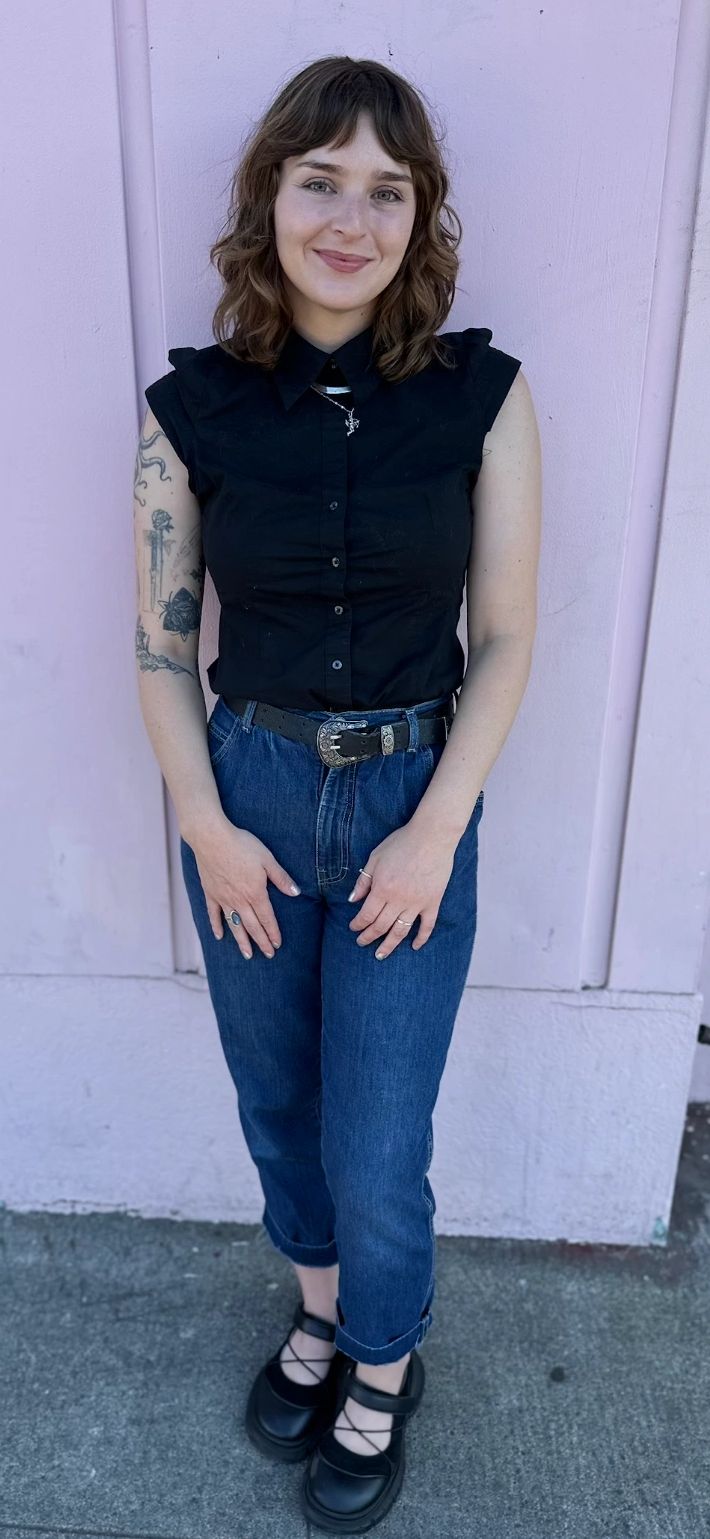 Young woman smiling, wearing a black sleeveless shirt and blue jeans.