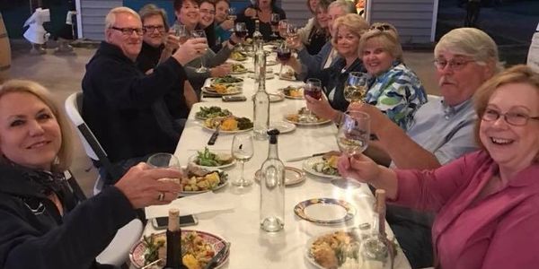 Picture of a long table with 14 smiling people sitting. They have raised glasses and are toasting.