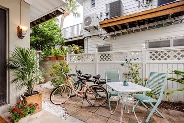 Cozy patio with bicycles, blue chairs, and green plants beside a white fence.