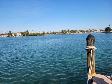 Calm waterfront with blue sky and dock post tied with rope.