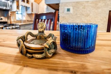 Brass octopus coaster holder with shell coasters next to a blue ribbed glass on a wooden table.