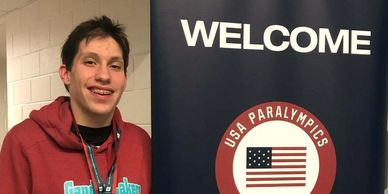 Nate standing wearing his gold medal next to a sign saying, "U.S. Paralympics National Championships