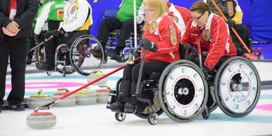 Athletes in wheelchairs practice curling on the ice.  