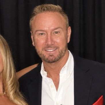 Man in a suit smiling, standing next to a woman.