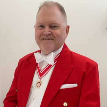 toastmaster Ian Wynne-Smythe in red jacket smiling