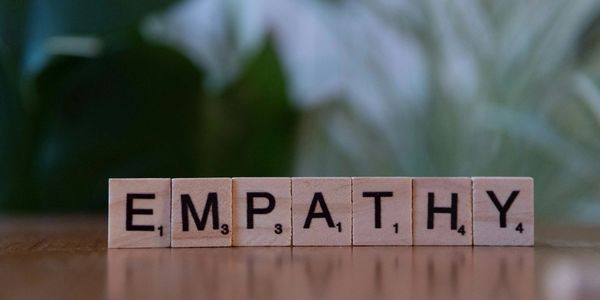 Scrabble tiles spell out "EMPATHY" on a wooden surface.