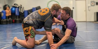Two men practicing Brazilian Jiu-Jitsu on a blue mat in a gym.