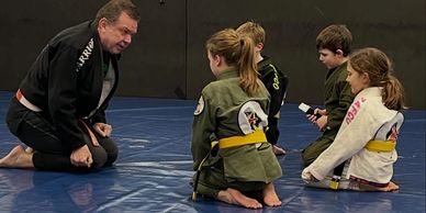 Martial arts instructor teaching four children on mats indoors.