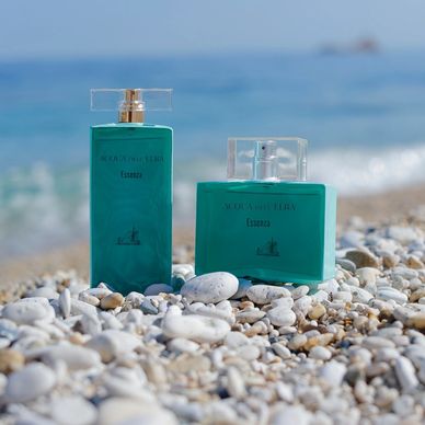 acqua dell elba Perfume and cologne sitting on a pebble beach with the beautifulocean in the back