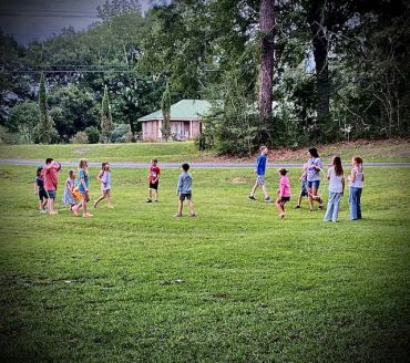 Children and adults playing outside on a grassy field.