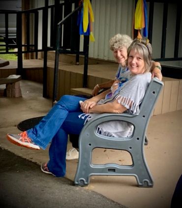 Two women smiling on a bench with colorful ribbons.