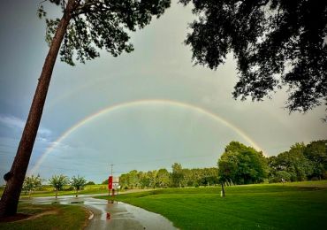 A rainbow arches over a green park after rain.