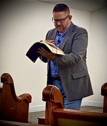Man reading a book in a church pew area.