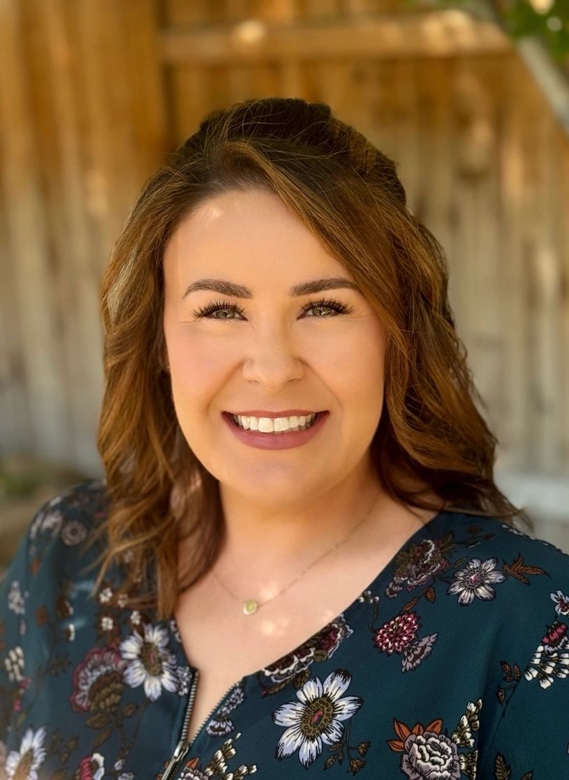 Smiling woman with curled hair and floral blouse.
