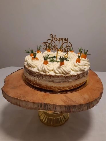 Rustic carrot birthday cake with creamy frosting and rosemary decorations on a wooden stand.