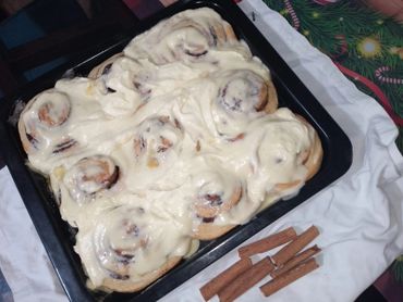 Freshly baked cinnamon rolls covered with creamy frosting on a baking tray.