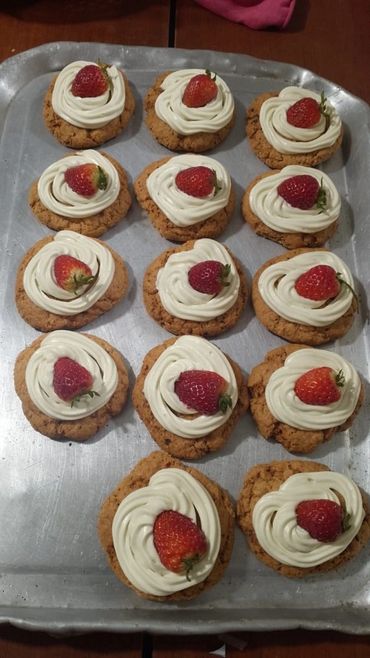 Oatmeal cookies topped with cream and fresh strawberries on a baking tray.