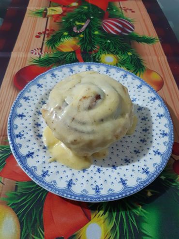 A cinnamon roll covered in creamy icing on a decorative plate.