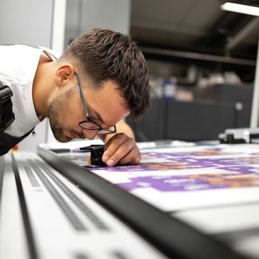 A man closely inspecting printed sheets with a magnifying tool in a print shop.