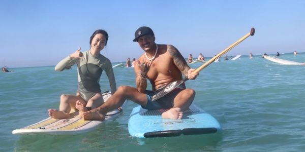 Two people posing on paddleboards in the ocean, smiling and making hand signs.