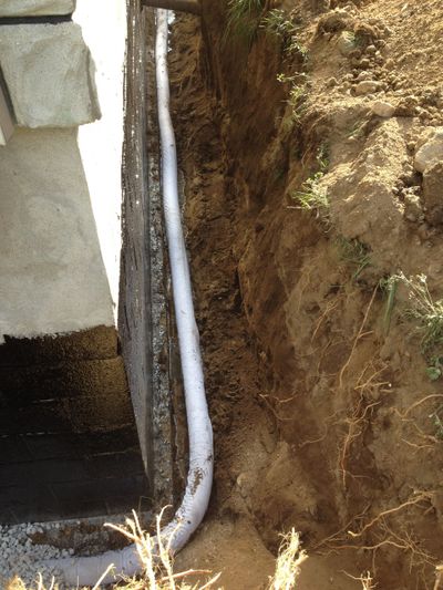 Deep trench beside house foundation with drainage pipe as part of basement waterproofing