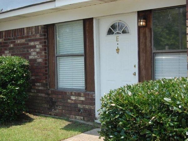 White door with letter E on a brick house surrounded by bushes.