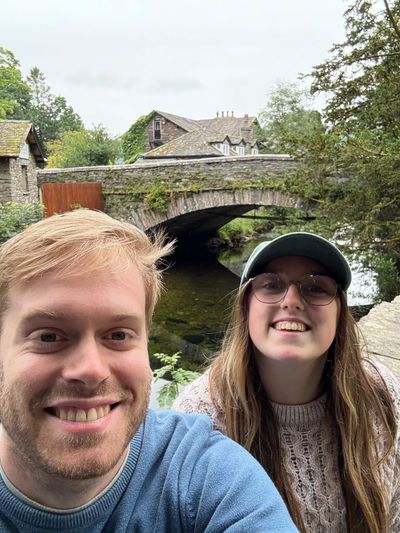 Happy couple taking a selfie near a stone bridge over a river.