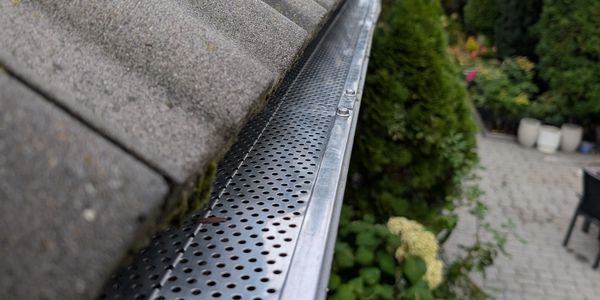 A close-up of a clean metal gutter guard on a tiled roof with greenery below.