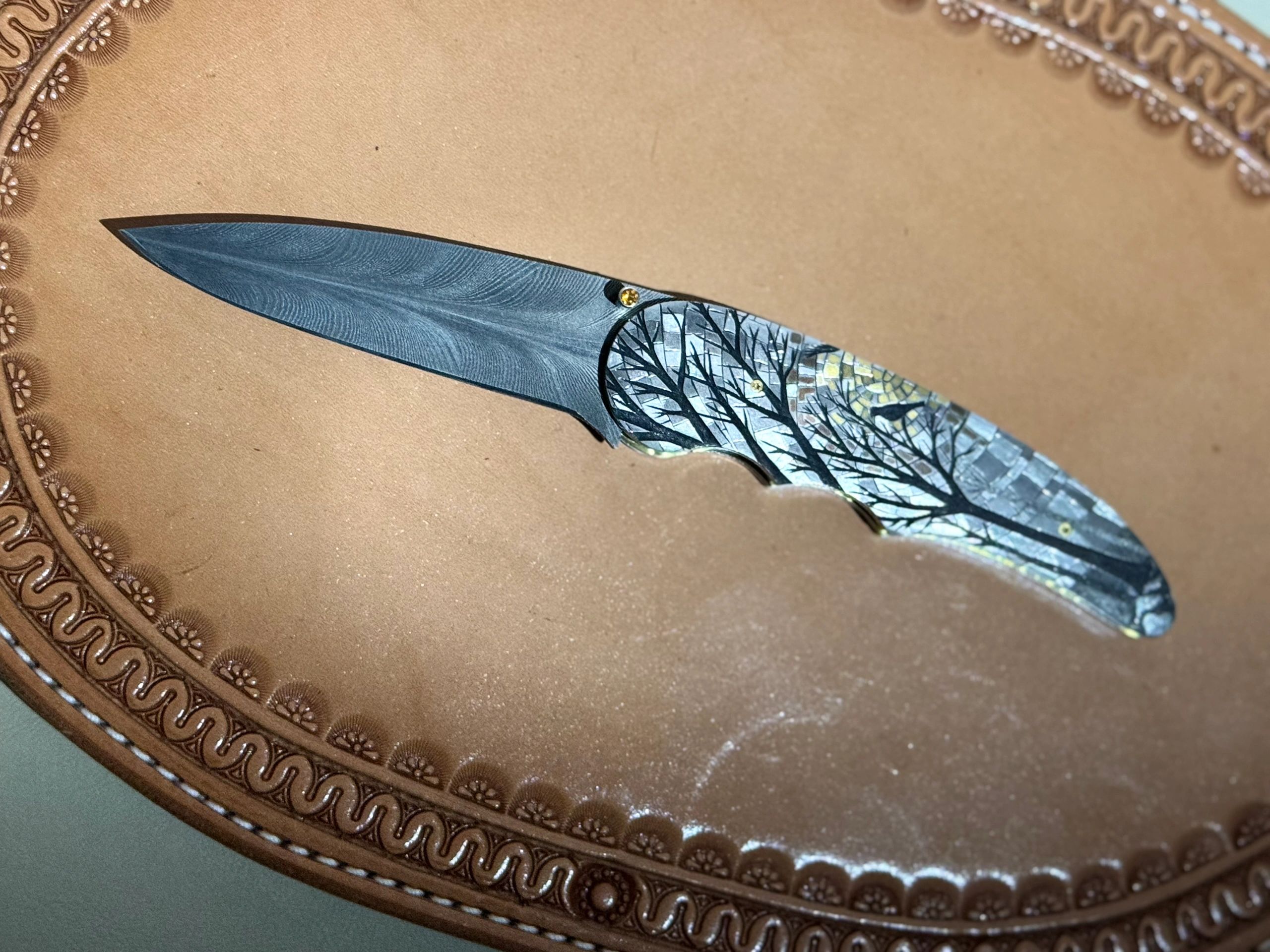 Decorative knife with intricate tree design on the handle, placed on an ornate leather surface.