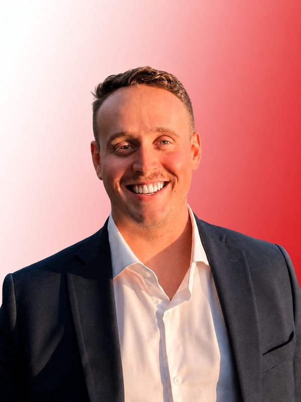 Smiling man in a dark suit and white shirt with a red gradient background.