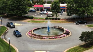 A roundabout with a central water fountain and surrounding flowers in a suburban area.