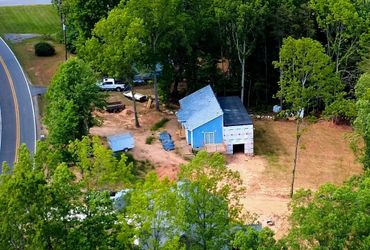 A partially built blue house surrounded by trees near a road.