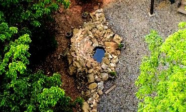A stone well surrounded by green trees and gravel ground.