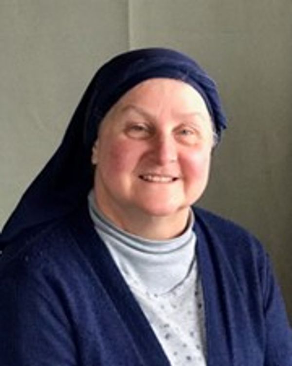 Smiling elderly woman wearing a dark headscarf and navy outfit.