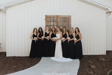 Bridesmaids and bride in black bridesmaids in front of the wooden doors to the reception hall.