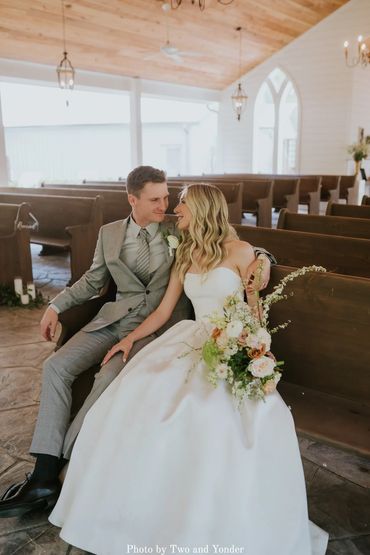 Bride and groom sitting on handcrafted pews at The Chapel at Firefly Lane wedding venue.