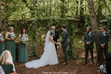 Bride and groom say their vows under a lush greenery floral arch in a forest wedding ceremony in TN.