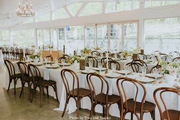 Wedding table layout and decor with white linens, wooden chairs and a beautiful glass venue.