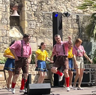 Dancers in lederhosen on wooden stage.