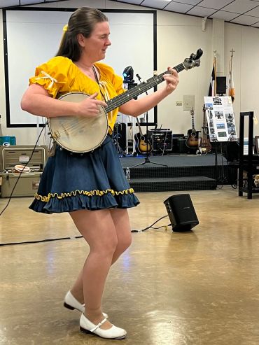 Lady in clogging costume playing banjo and dancing