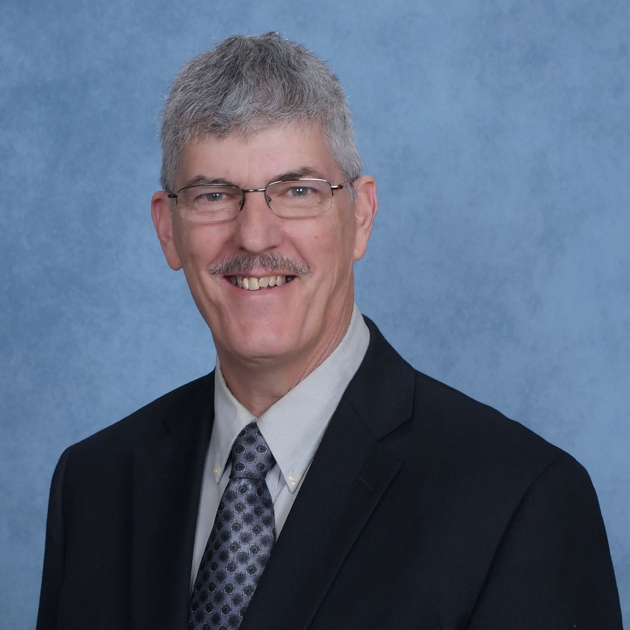 Smiling man in suit and glasses against a blue background.