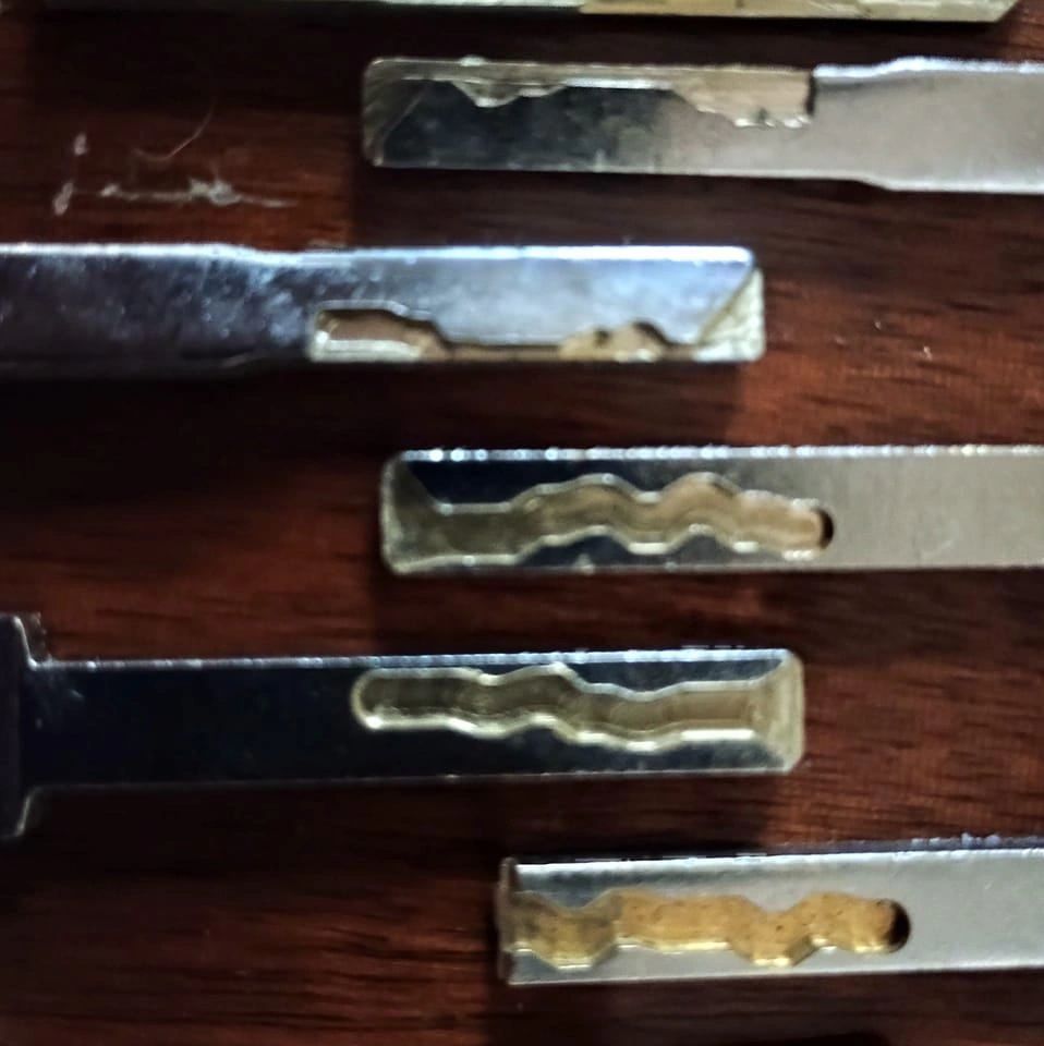Close-up of several metallic locksmith lock picks on a wooden surface.