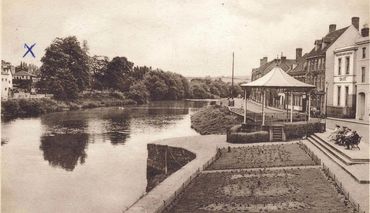 Vintage riverside town scene with people sitting by a bandstand near a riverbank.