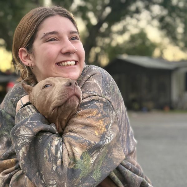 A joyful person hugs a brown puppy outdoors.